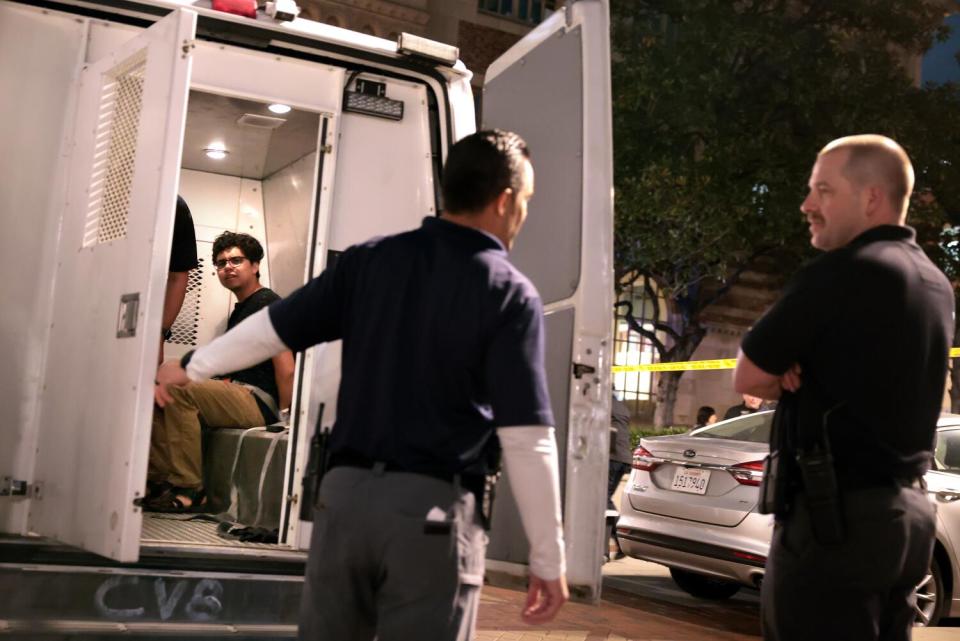 An arrested person is seen in the open back of a van.