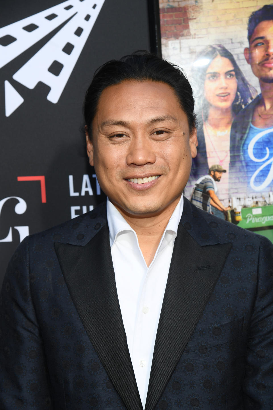 Jon M. Chu at a red carpet event, dressed in a patterned blazer and white shirt