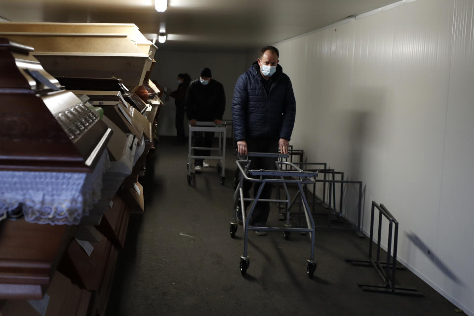 Workers walk past caskets placed inside an overflow cold storage container placed outside a crematorium in Ostrava, Czech Republic, Thursday, Jan. 7, 2021. The biggest crematorium in the Czech Republic has been overwhelmed by mounting numbers of pandemic victims. With new confirmed COVID-19 infections around record highs, the situation looks set to worsen. Authorities in the northeastern city of Ostrava have been speeding up plans to build a fourth furnace but, in the meantime, have sought help from the government’s central crisis committee for pandemic coordination. (AP Photo/Petr David Josek)