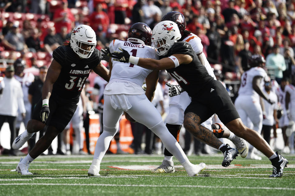 Virginia Tech quarterback Kyron Drones (1) is sacked by Louisville defensive lineman Stephen Herron (14), right, and defensive back Marcus Washington (31) during the first half of an NCAA college football game in Louisville, Ky., Saturday, Nov. 4, 2023. (AP Photo/Timothy D. Easley)