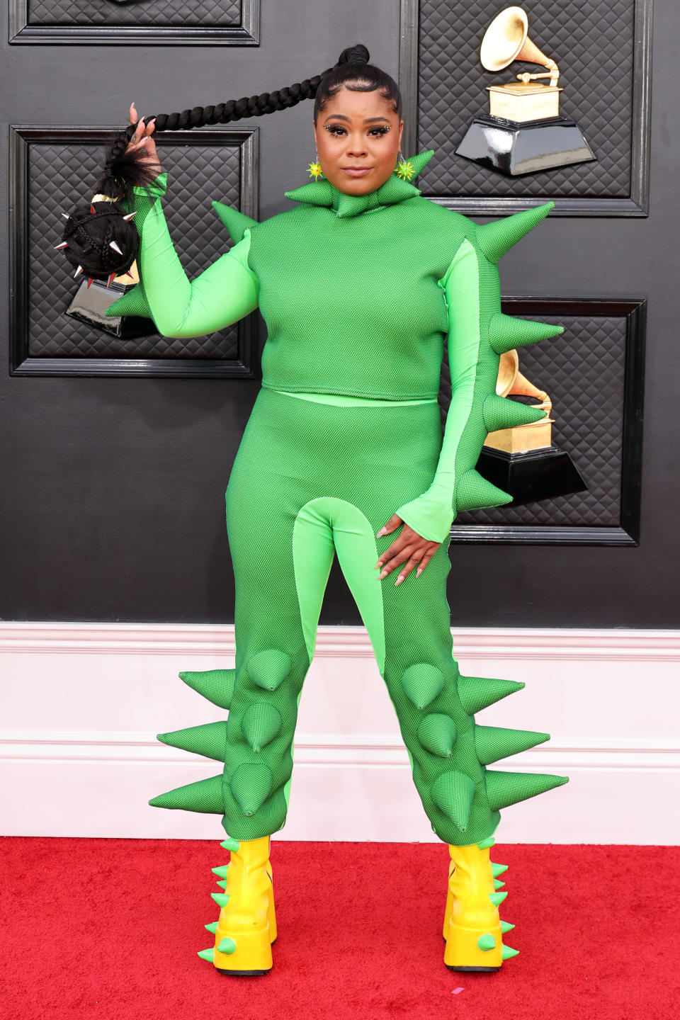 Tayla holding her long braid and wearing a dinosaur-esque outfit on the red carpet