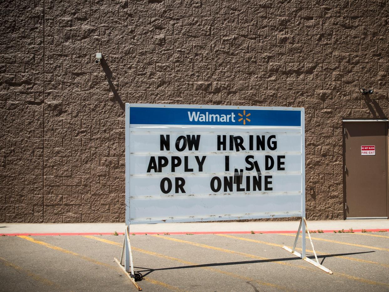 A sign outside a Walmart says, "Now hiring. Apply inside or online."