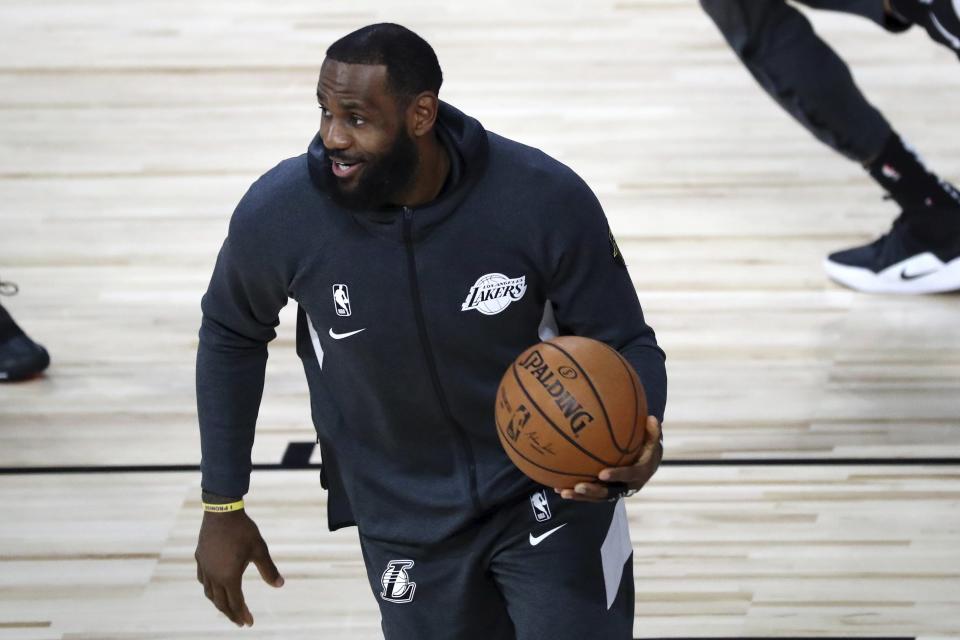 LeBron James in a black warm-up jacket holds a basketball on a court. 