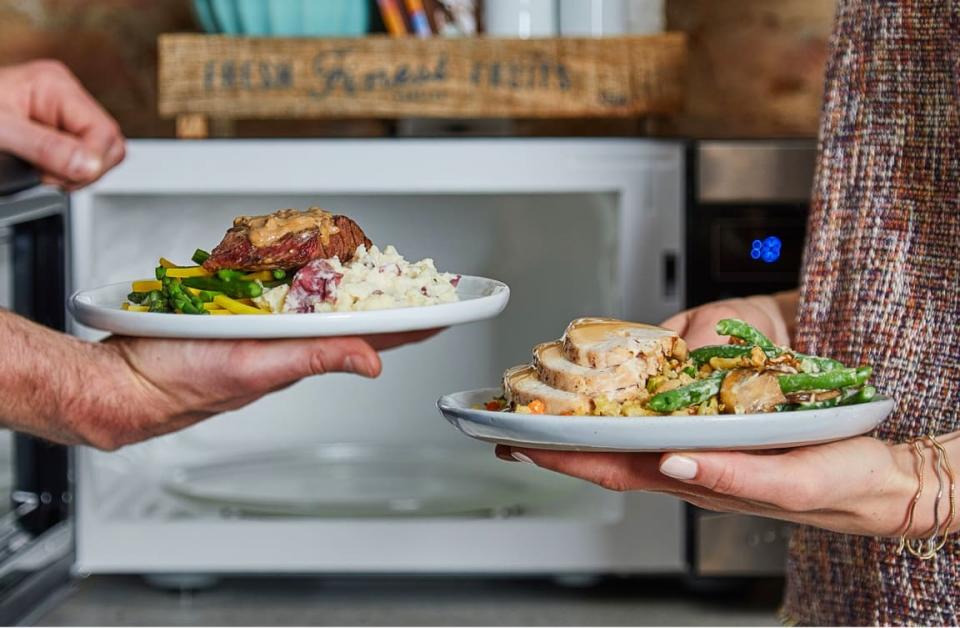 two people holding plates of food in front of a microwave