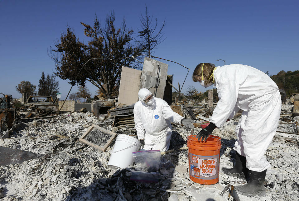 FILE - In this Tuesday, Oct. 31, 2017, file photo, David Rust, left, and his wife Shelly search through the remains of their home destroyed by wildfires in Santa Rosa, Calif. Attorneys representing 14 local governments said Tuesday, June 18, 2019, that they had reached a $1 billion settlement with California utility Pacific Gas & Electric for a series of fires dating to 2015. (AP Photo/Jeff Chiu, File)