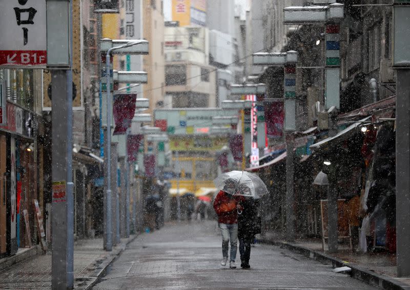A couple wearing protective face masks walks on a nearly empty street in a snow fall during a coronavirus disease outbreak in Tokyo