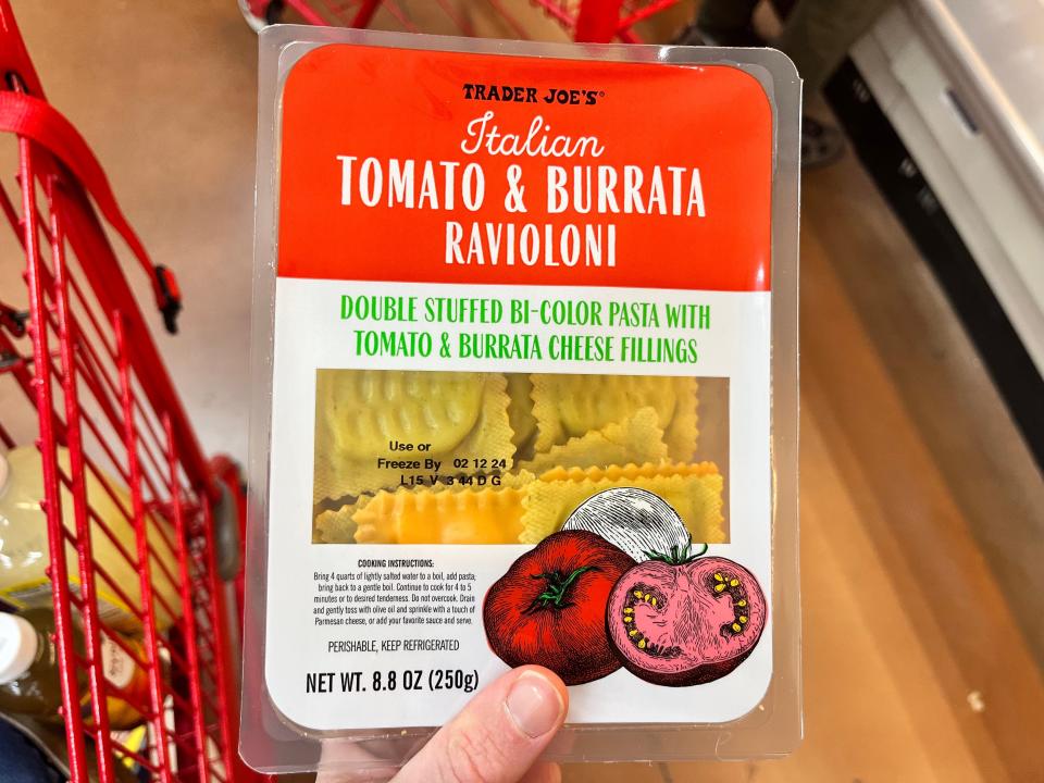 A hand holding a package of Trader Joe's Italian tomato and burrata ravioloni.