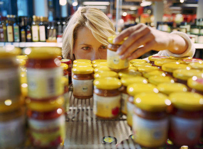 A person is organizing jars of food on a supermarket shelf, focusing on arranging them neatly