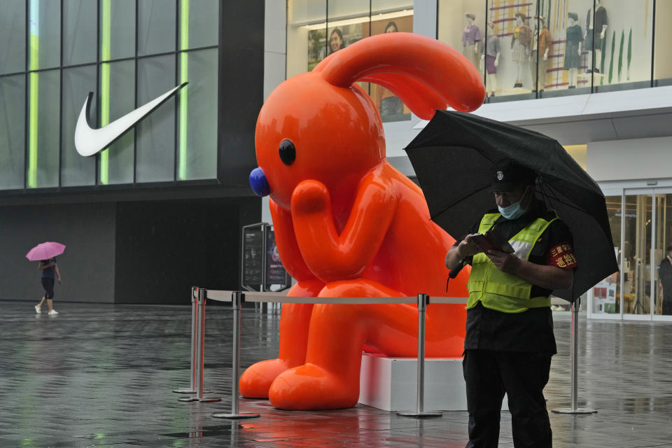 A security guard holds an umbrella as he stands near an art work outside a mall during a rainy day in Beijing, Sunday, Aug. 14, 2022. (AP Photo/Ng Han Guan)