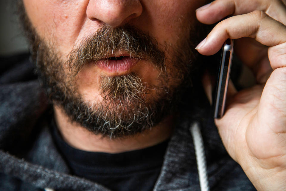 Close up portrait of bearded man talking on smart phone, focus on lips, no eyes, secret talk, criminal threating someone