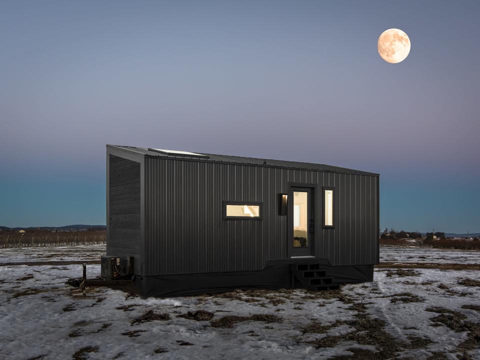 a black tiny home with windows  on a snowy field at sunset