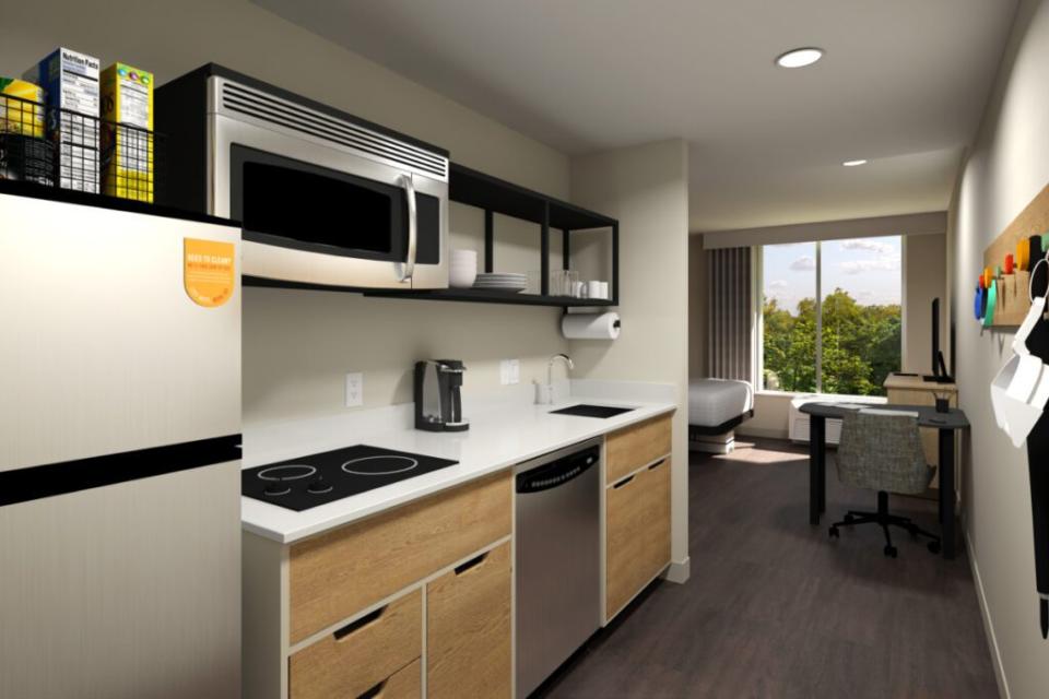 Hilton in 2023 announced a new extended-stay hotel brand without yet an official name. Here's a photo-illustration of a guest room, Ample storage space, efficient closet design, and movable, multi-purpose furniture enable guests to seamlessly enjoy the space as both a place to work and rest. This includes a fully equipped kitchen with a full-sized refrigerator, dishwasher, microwave, and a two-burner stovetop. Source: Hilton.