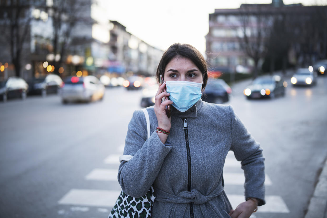 Woman with mask talking on the phone, she walking on crossroad in the city.