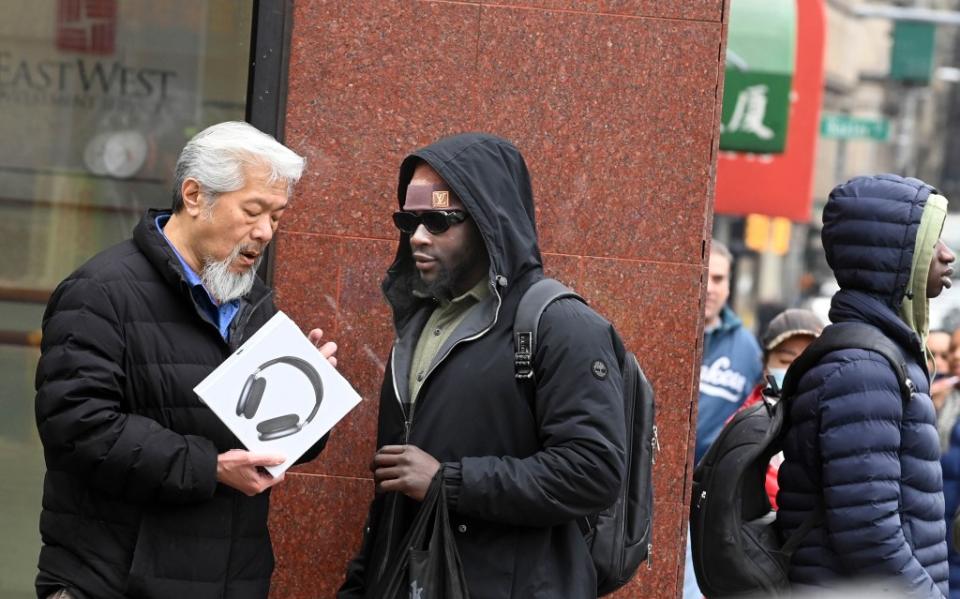 Chinatown activist Karlin Chan barters with a peddler trying to sell him a knockoff AirPods Max headphones. Helayne Seidman