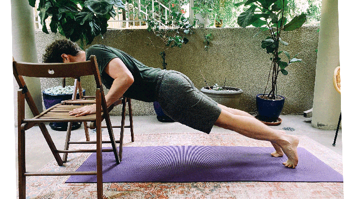 Man practicing Chaturanga, or a half push-up, with his hands on two chairs on his yoga mat