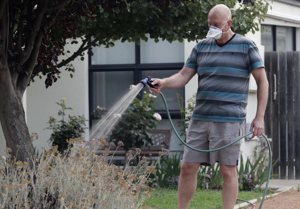 FILE - In this Jan. 2, 2020, file photo, a man waters his garden while wearing a mask as smoke shrouds the Australian capital of Canberra, Australia. It's an unprecedented dilemma for Australians accustomed to blue skies and sunny days that has raised fears for the long-term health consequences if prolonged exposure to choking smoke becomes the new summer norm. (AP Photo/Mark Baker, File)