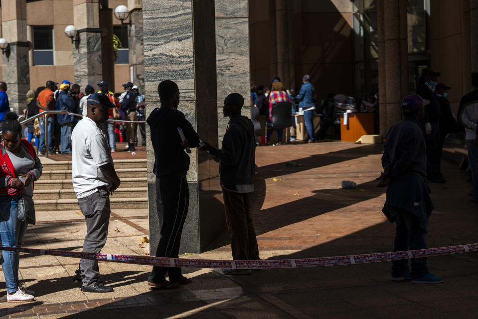 Informal vendors line up to receive temporary working licenses, at the entrance of a municipal office building, in Johannesburg, Tuesday, April 7, 2020. South Africa and more than half of Africa's 54 countries have imposed lockdowns, curfews, travel bans or other restrictions to try to contain the spread of COVID-19. (AP Photo/Jerome Delay)