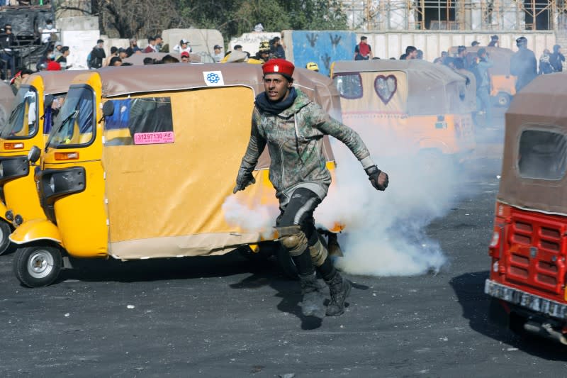 An Iraqi demonstrator runs as he carries a tear-gas canister during ongoing anti-government protests, in Baghdad