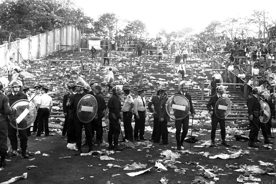 File - In this May 29, 1985 file photo, Belgian riot police stand in a line in front of debris littered stands, after a disastrous clash between rival soccer fans during the European Cup Final at the Heysel Stadium in Brussels. Friday, May 29, 2020 marks 35 years since 39 victims lost their lives during a European Cup football match between Liverpool and Juventus due to a surge of rival supporters resulting in a collapsed wall. (AP Photo, File)