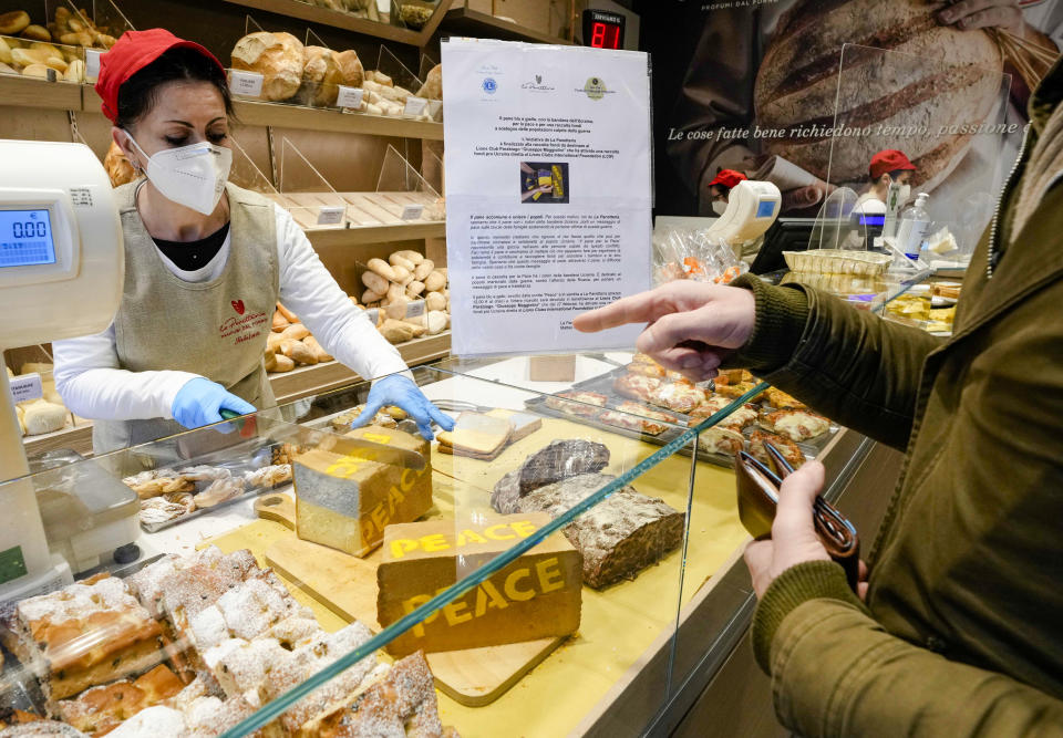 A shop attendant sells the 'bread for peace' made by baker Matteo Cunsolo in Parabiago near Milan in northern Italy, Thursday, March 17, 2022. Cunsolo used saffron and the infusion of a Thai plant to make a bicolor loaf of bread with the colors of the Ukraine national flag and butter-sprayed the word 'peace' on its sides in solidarity with the war-battered country. (AP Photo/Luca Bruno)