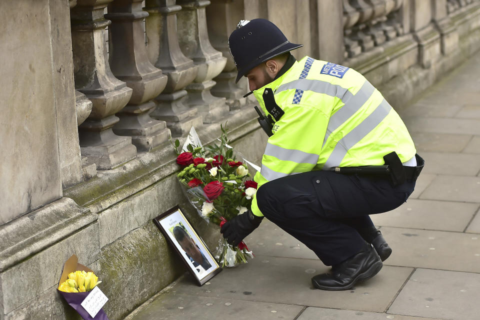 A police officer places flowers and a photo of fellow police officer Keith Palmer, who was killed in yesterdays attack, on Whitehall near the Houses of Parliament in London, Thursday March 23, 2017. On Wednesday a knife-wielding man went on a deadly rampage, first driving a car into pedestrians then stabbing a police officer to death before being fatally shot by police within Parliament's grounds in London. (Dominic Lipinski/PA via AP)