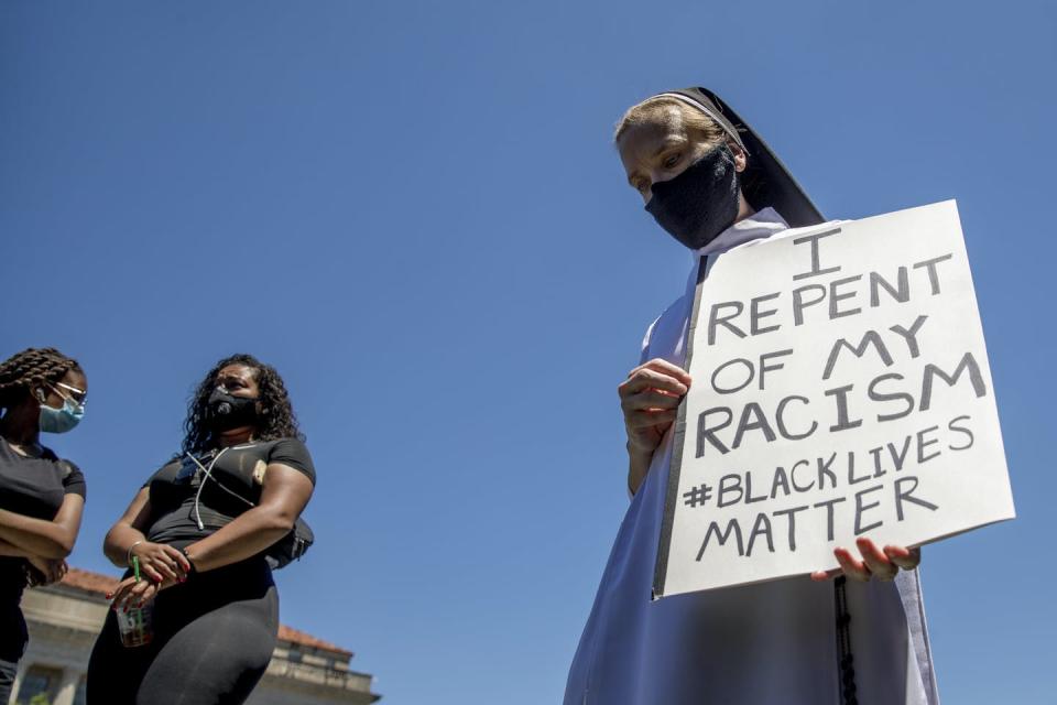 A woman holds a sign that reads I Repent of my Racism #blacklivesmatter as she prays.