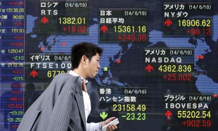 A pedestrian holding his mobile phone walks past an electronic board showing the stock market indices of various countries outside a brokerage in Tokyo June 19, 2014. REUTERS/Yuya Shino