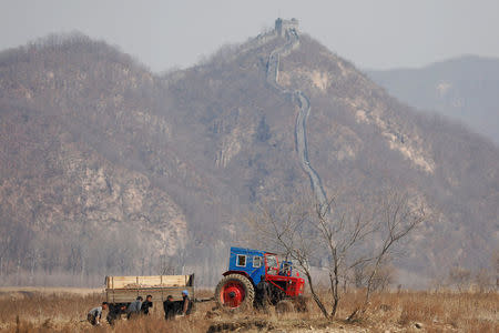 North Korean farmers work in a field as a section of the Great Wall is seen on the Chinese side of the Yalu River, north of the town of Sinuiju in North Korea and Dandong in China's Liaoning province, April 2, 2017. REUTERS/Damir Sagolj