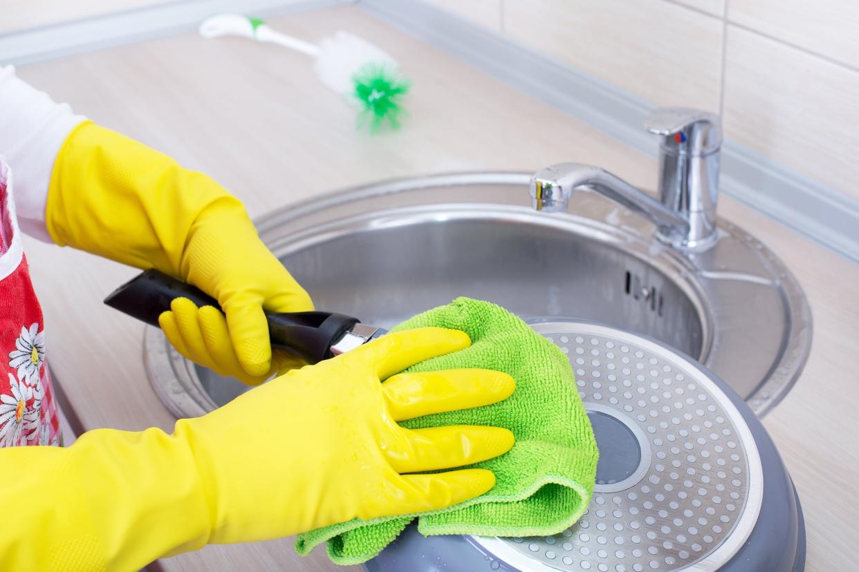 close up of female hands with rubber gloves cleaning frying pan in the kitchen