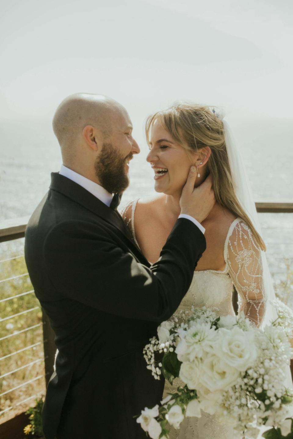 A groom holds his bride's neck as they smile at each other.