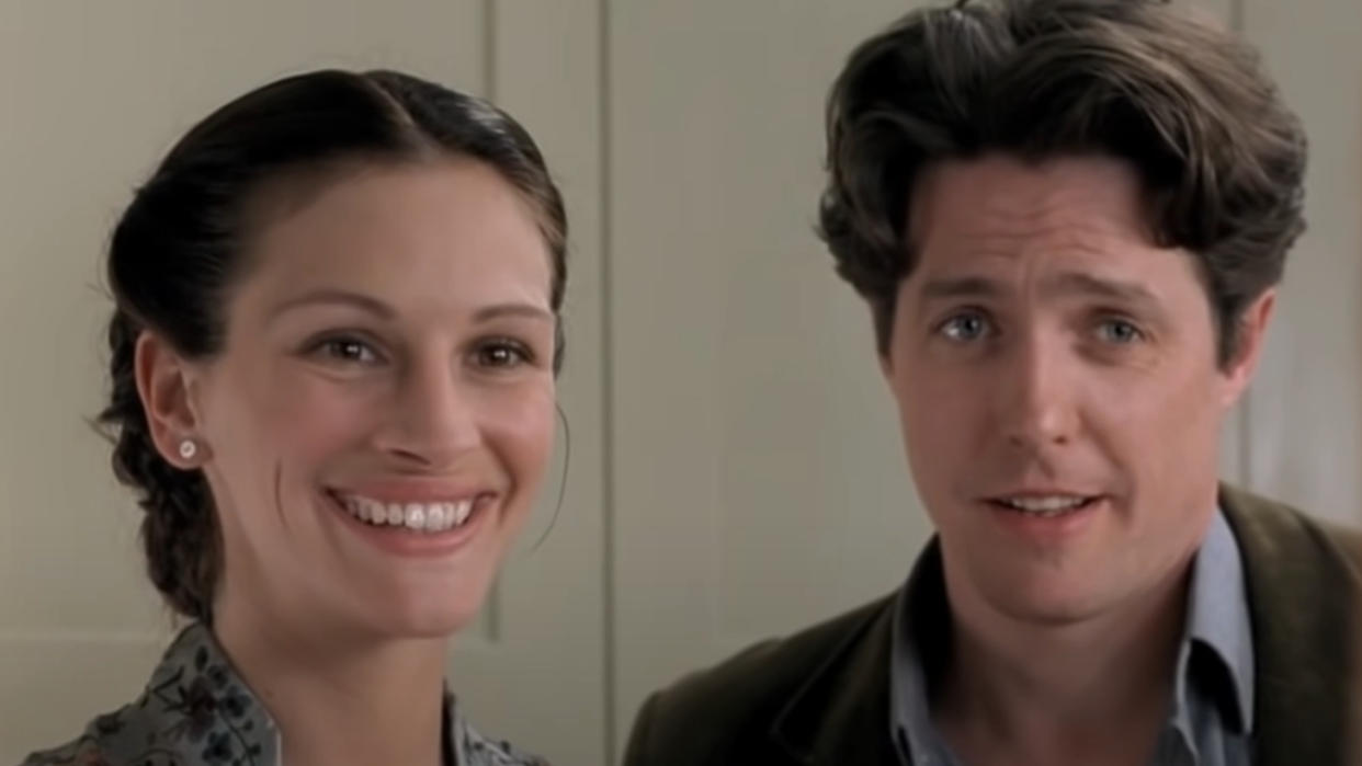  Julia Roberts and Hugh Grant stand smiling together in Notting Hill.  