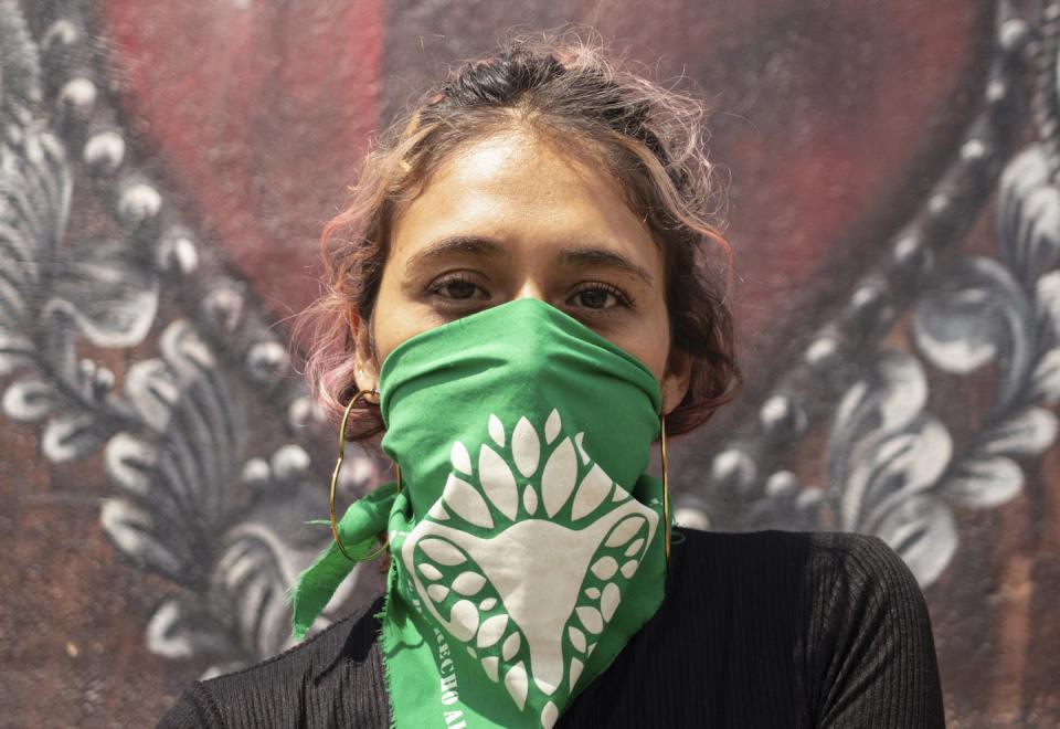 A young Latina woman wears a green bandana over her nose and mouth
