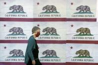 FILE - In this Thursday, April 30, 2020, file photo, a pedestrian wearing a mask walks in front of a billboard displaying California flags in San Francisco during the coronavirus outbreak. California's death count from the coronavirus surpassed 15,000 on Sunday, Sept. 20, 2020 even as the state saw widespread improvement in infection levels. (AP Photo/Jeff Chiu, File)