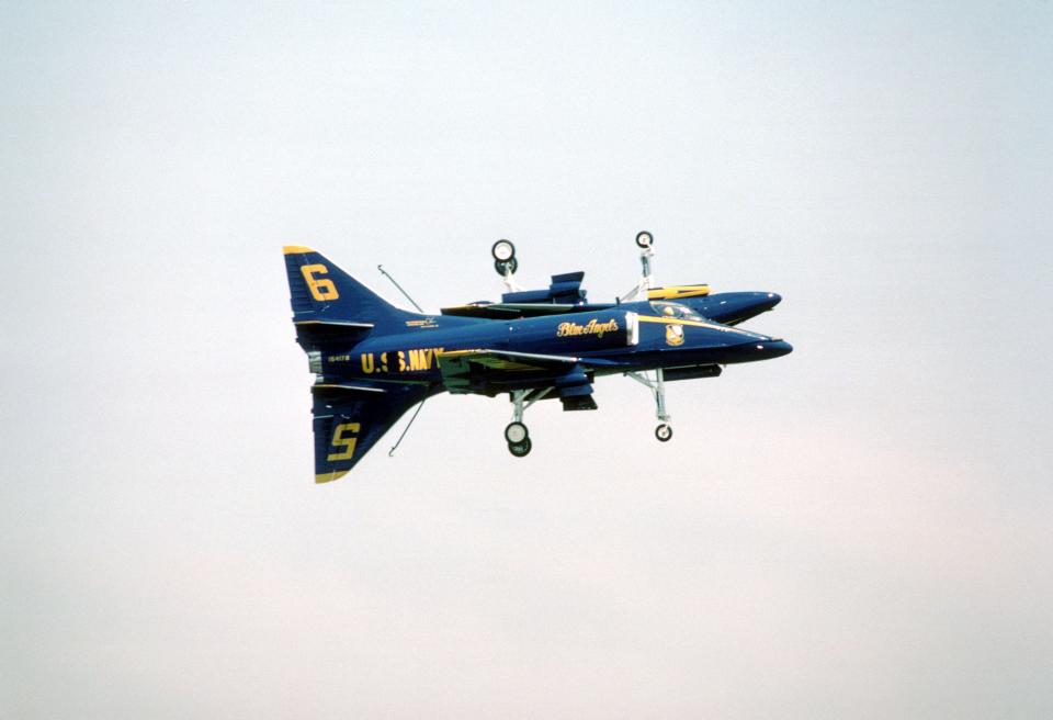 Two Blue Angels Flight Demonstration Squadron A-4F Skyhawk II aircraft execute the "Fortus" maneuver during an air show. In this wingtip-to-wingtip maneuver, both aircraft have their landing gear and tail hooks lowered and one aircraft is inverted.