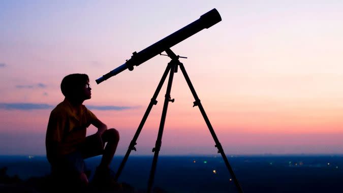 A young boy looking thru a telescope at sunset.