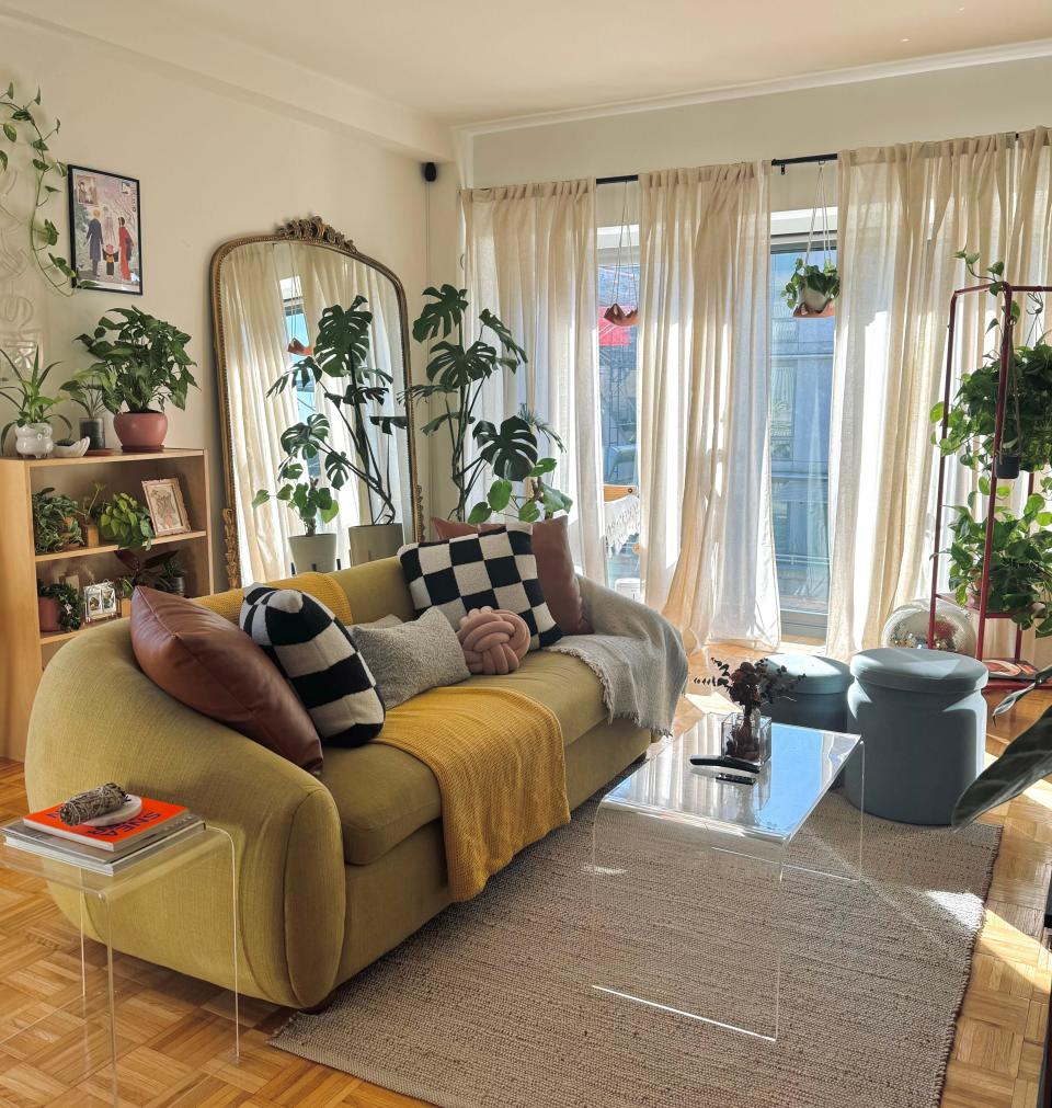 A living room with a yellow sofa and lots of house plants.