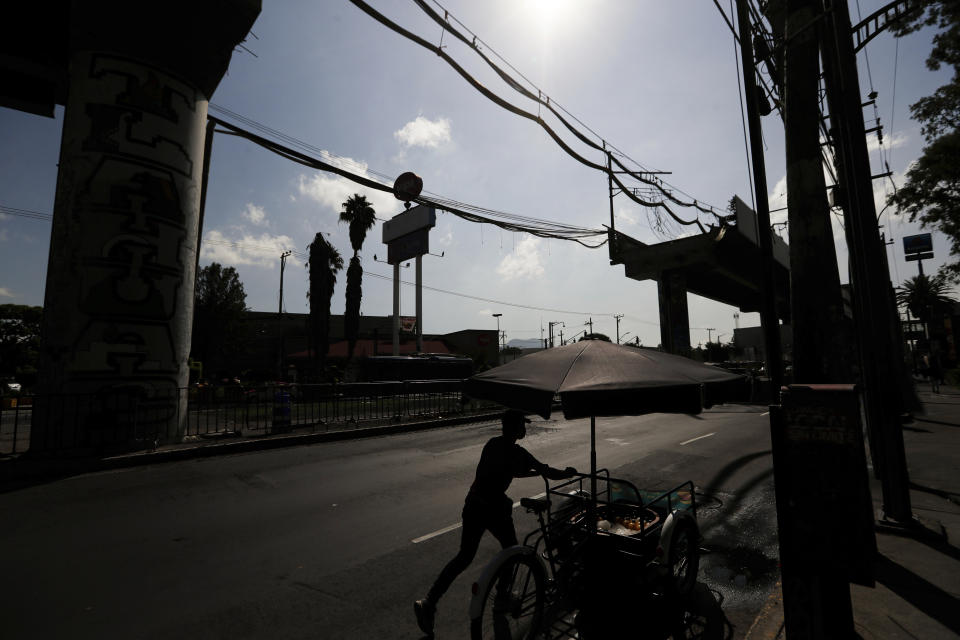 A vendor pushes his bicycle past the missing section of an elevated metro in Mexico City, Wednesday, June 16, 2021. A June 16, 2021, preliminary report by experts into the collapse that killed 26 people placed much of the blame on poor welds in studs that joined steel support beams to a concrete layer supporting the trackbed. (AP Photo/Fernando Llano)