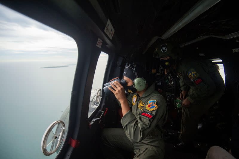 An Indonesian Air Force personnel looks through the window of NAS-332 Super Puma helicopter during an aerial search for the Sriwijaya Air SJ-182, which crashed to the sea