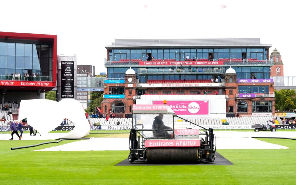 Ground staff attempt to clear the water off the field during day two of the First Rothesay Test match at the Emirates Old Trafford, Manchester