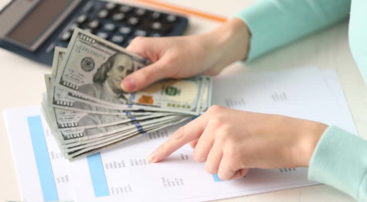 A photo of a person holding money while reading statistics on a page.