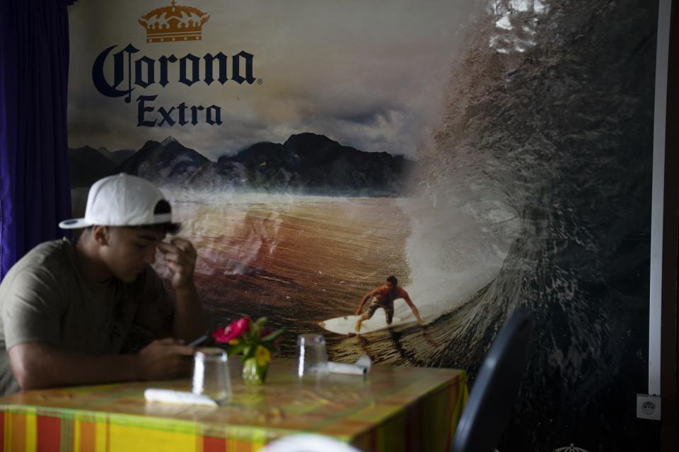 A customer sits at the only snack bar in the village of Teahupo'o, Tahiti, French Polynesia, Monday, Jan. 15, 2024. (AP Photo/Daniel Cole)