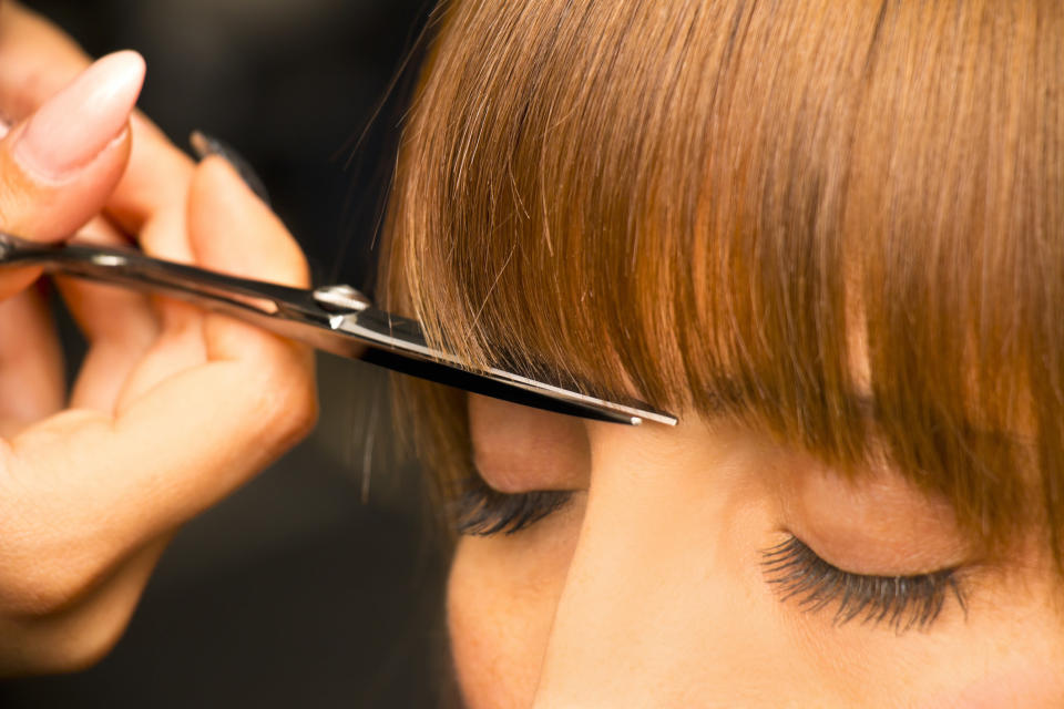 A hand holding scissors cuts bangs into someone's hair