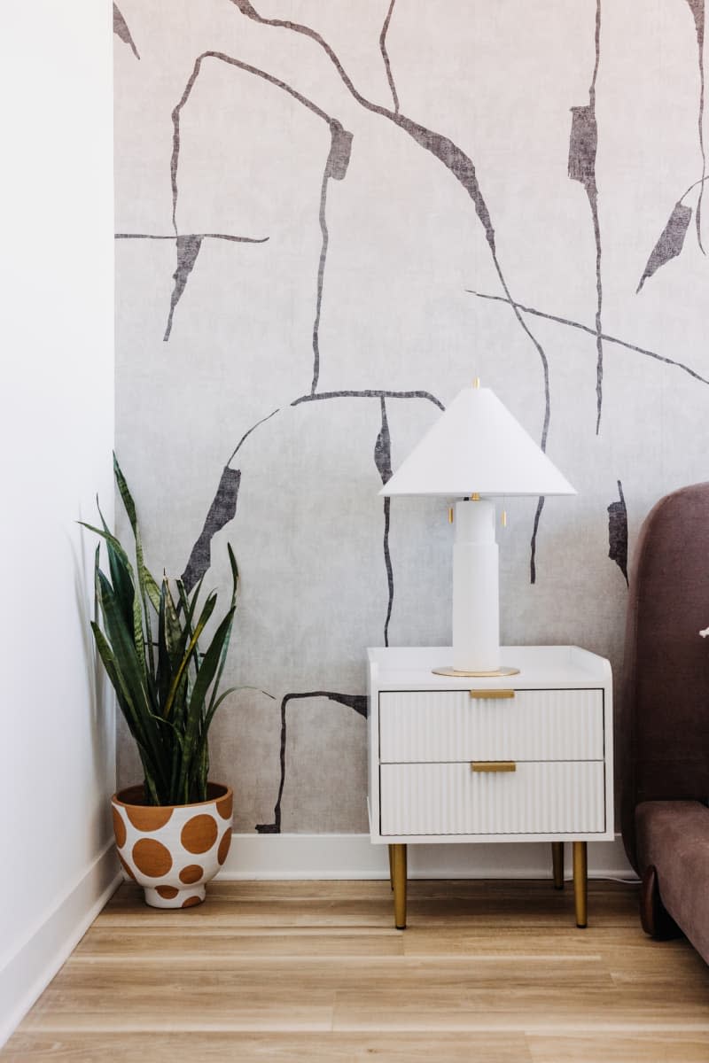 detail of white fluted bedside table and modern white lamp with gray and white patterned wallpaper behind