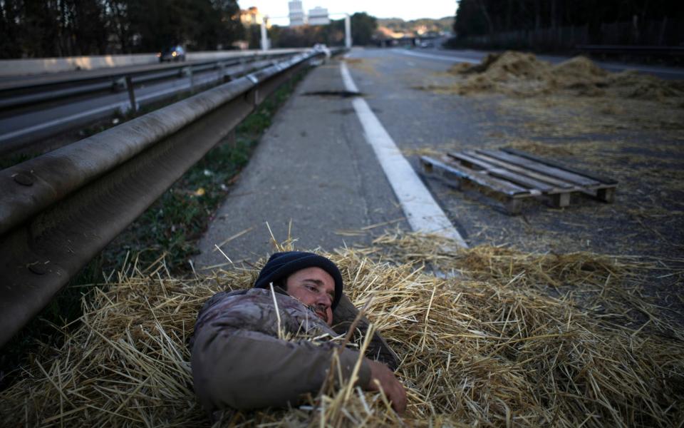 A farmer lies in a pile of hay after spending the night at a highway barricade in Aix-en-Provence, southern France