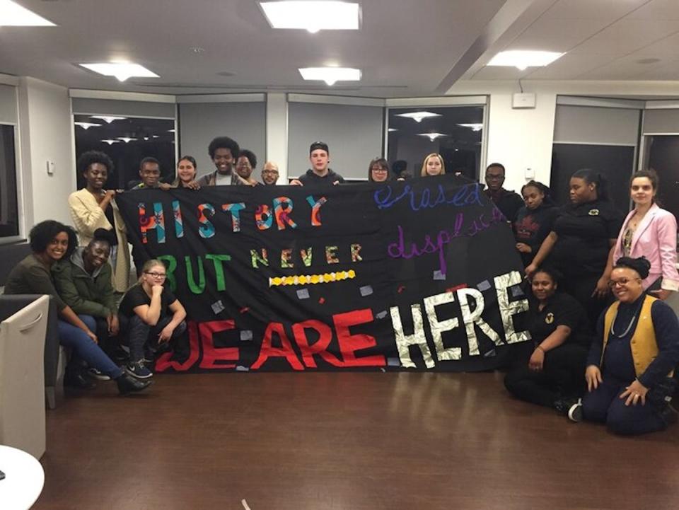 Eve Tuck and Tkaronto CIRCLE Lab youth researchers and collaborators hold a hand-made banner that reads: ‘History erased but never displaced. WE ARE HERE.’ (Eve Tuck), Author provided
