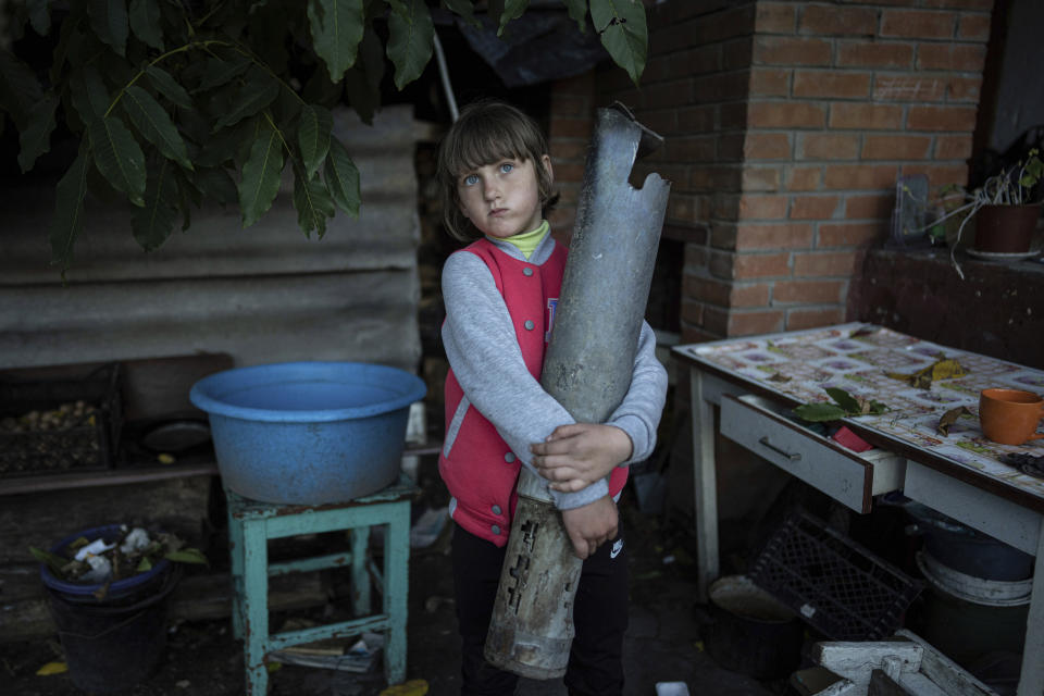 Veronika Tkachenko, 7, holds a piece of a Grad rocket which hit her family's house in the recently retaken town of Izium, Ukraine, Sunday, Sept. 25, 2022. (AP Photo/Evgeniy Maloletka)