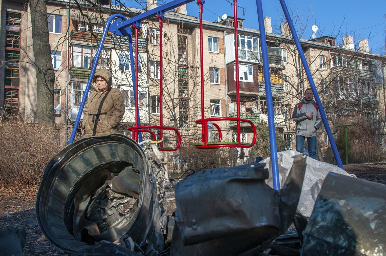 A man and woman stand next to fragments of military equipment on the street in the aftermath of an apparent Russian strike in Kharkiv in Kharkiv, Ukraine, Thursday, Feb. 24, 2022.