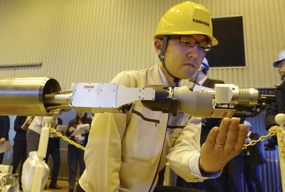 Toshiba Corp.'s energy systems unit group manager Jun Suzuki shows a remote-controlled melted fuel probe device at its facility in Yokohama, near Tokyo, Monday, Jan. 28, 2019. Toshiba unveiled the device carrying tongs that comes out of a long telescopic pipe for an internal probe in one of three damaged reactor chambers at Japan’s tsunami-hit Fukushima nuclear plant - this time to touch chunks of melted fuel. (AP Photo/Mari Yamaguchi)