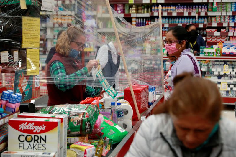 FILE PHOTO: A cashier serves customer behind a makeshift plastic barrier as a preventive measure against the spread of the coronavirus disease (COVID-19) at Garis supermarket in Toluca