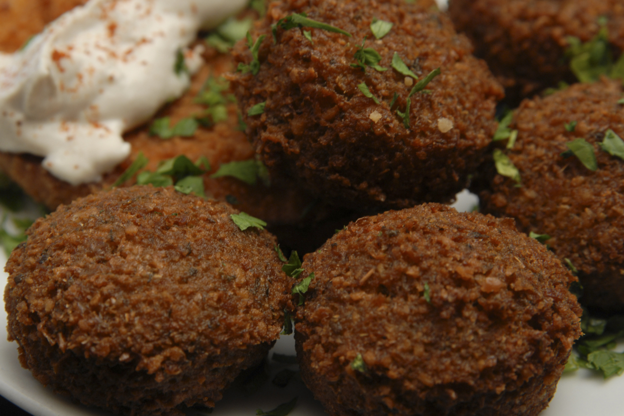 Closeup of many Easy Vegan Falafels, selective focus, on a white plate, tahini sauce on a vegan fried chicken piece blurred in the background